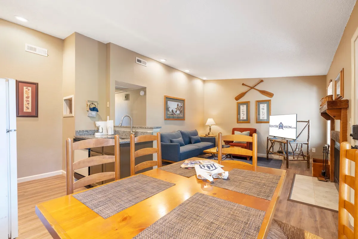 This interior shot features an inviting open-concept layout with a dining table, blue sofa, fireplace, and a television. The warm and welcoming atmosphere is accentuated by cozy furnishings, making it ideal for gatherings and relaxation.