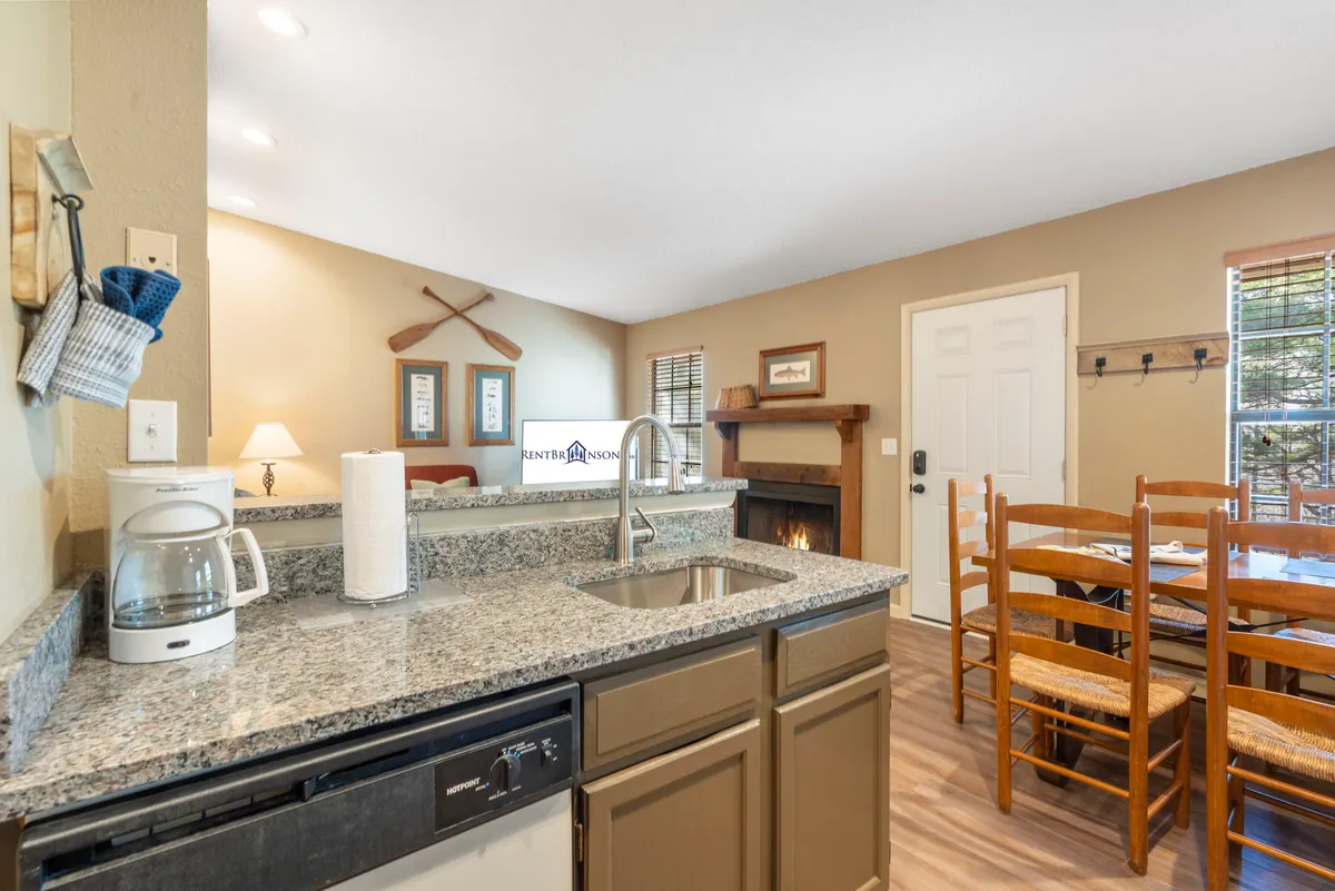 A cozy, inviting interior space showcasing a kitchen counter, dining table, and a fireplace, all warmly lit and decorated. The scene suggests intimate dinners and winding down together after a day of exploring.