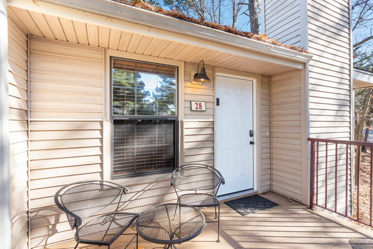 The image captures the front door of unit 28, flanked by a pair of outdoor chairs, surrounded by greenery. The atmosphere is inviting and relaxed, with the number 28 clearly displayed, highlighting the specific unit.