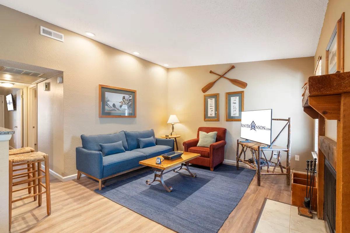 A cozy living room featuring a blue sofa (which also functions as a sleeper sofa), red armchair, wooden coffee table, and decorative paddles on the wall. The setting is ideal for socializing, reading, or accommodating extra guests.
