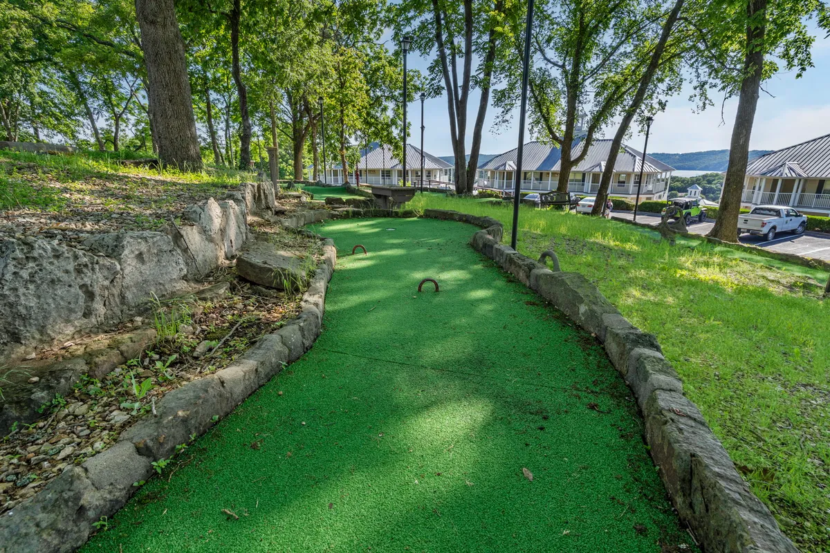 A playful mini-golf course nestled among green turf, rocky outcrops, and shady trees. The scene feels lighthearted and fun, with groups gathered for laughter and friendly competition. Natural elements create a relaxed, family-friendly vibe.