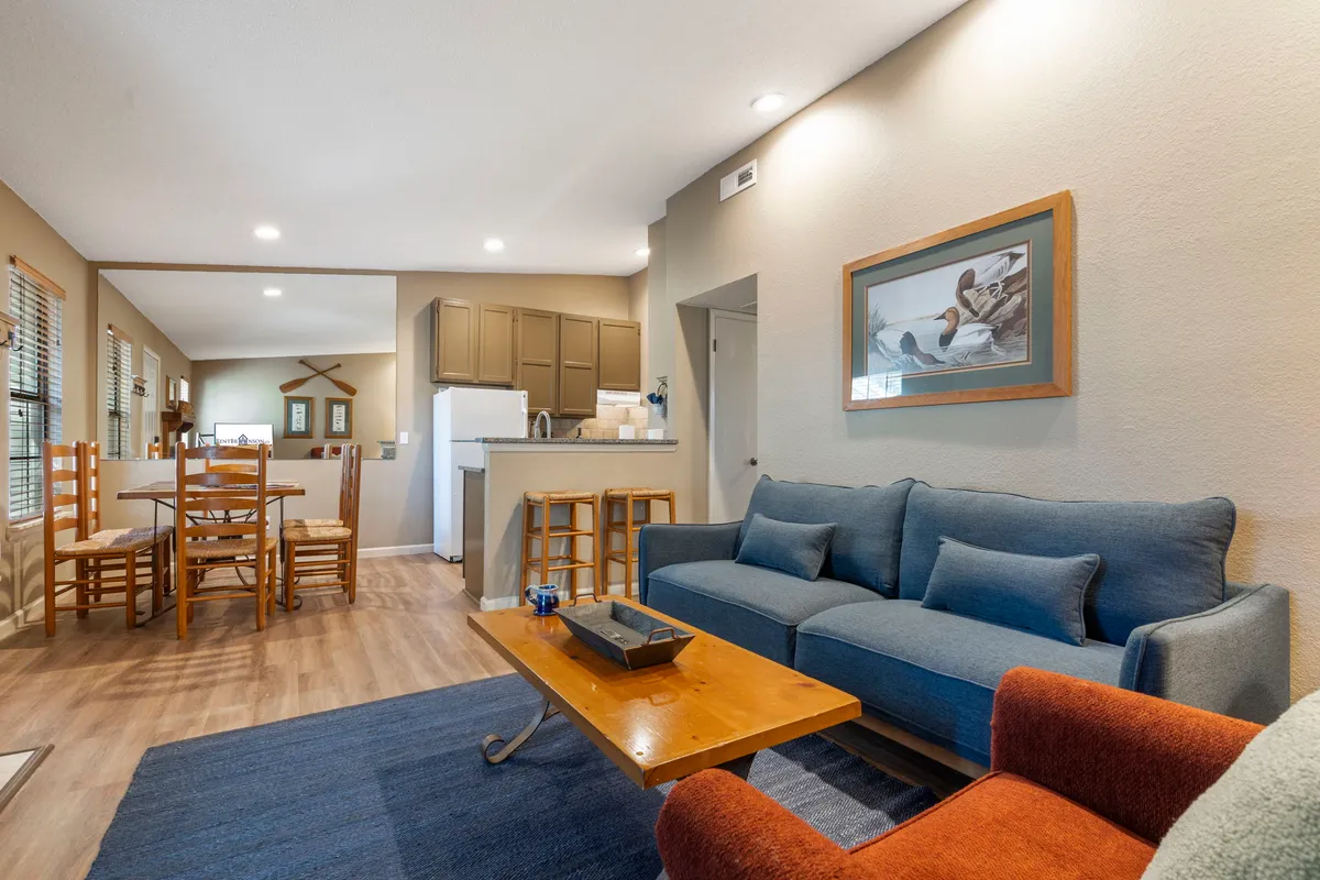 The image showcases a comfortable homey interior highlighted by a plush sofa, dining table, kitchen area, and tasteful wall art. The space is set up for both relaxation and communal dining, echoing the theme of shared moments.