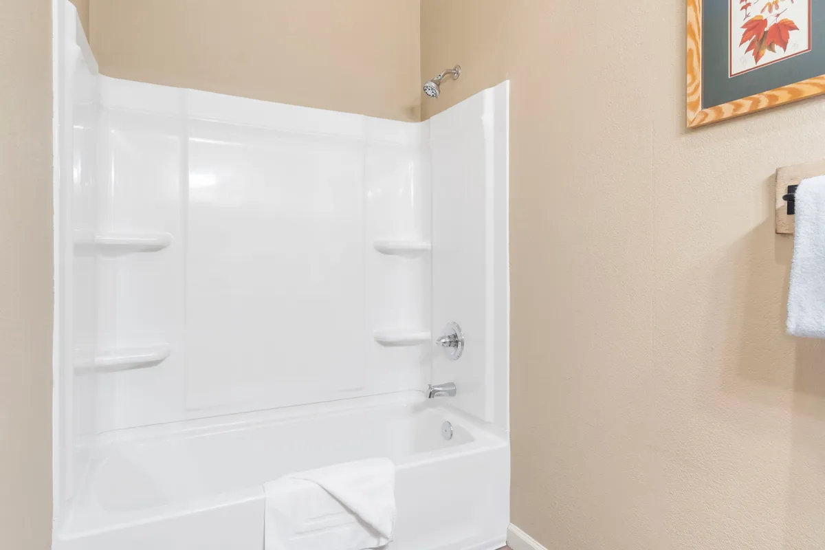 A modern bathroom with a spacious bathtub, shower area, decorative wall art, and a towel rack, all styled in calming tones. The room suggests a spa-like experience for self-care and relaxation.