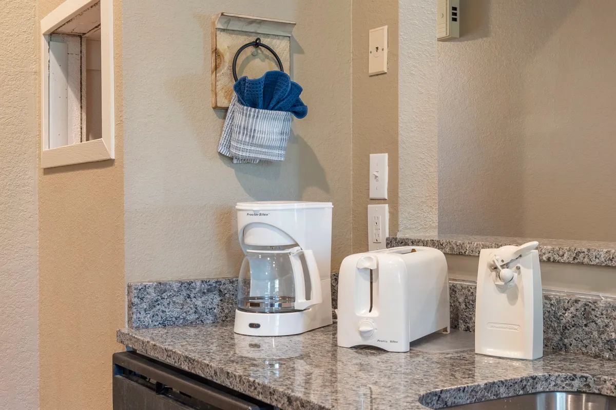 A close-up of the kitchen counter featuring a coffee maker, toaster, kitchen towel, and sleek granite countertop. The arrangement is inviting for anyone interested in making breakfast or enjoying a fresh cup of coffee.