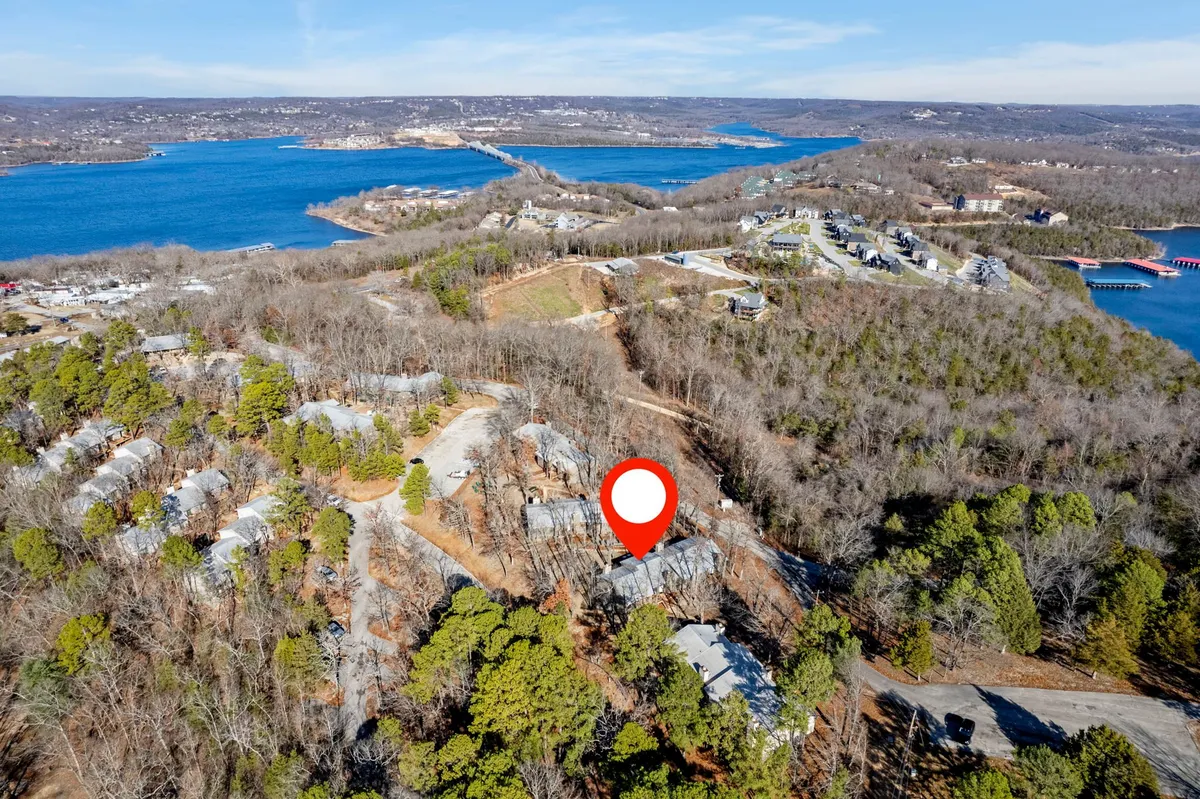 A peaceful lakeside scene featuring wooded areas, a view of the lake, and residential structures nestled among the trees. The landscape looks perfect for walking, hiking, or relaxing by the water.