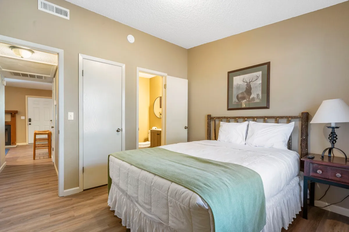 A cozy queen-sized bed with a nightstand and lamp, accented by framed artwork on the wall. The room feels warm and comfortable, offering a quiet place to relax and recharge.