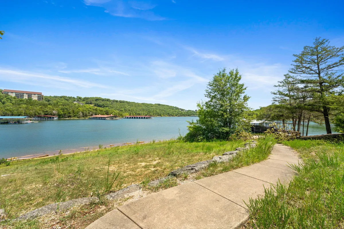 This image features a scenic view of Table Rock Lake with a winding pathway leading down to the shoreline, surrounded by lush greenery and distant hills. The foreground beckons visitors toward the water for activities such as fishing, boating, or simply enjoying a lakeside picnic. The tranquil mood is enhanced by the golden light, hinting at the serenity of sunset or early evening.
