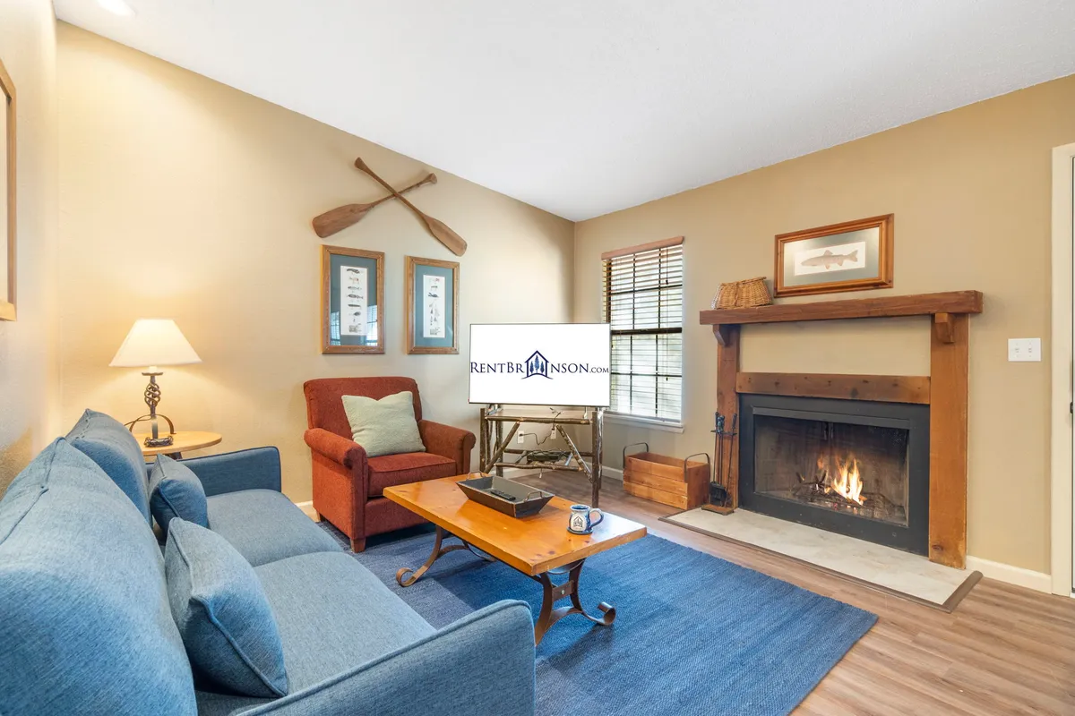 The image showcases a cozy, tastefully decorated living area featuring a plush sofa, a glowing fireplace as the centerpiece, a modern coffee table, and an inviting armchair. Subtle wall decor adds charm, while the warm lighting sets an inviting mood perfect for unwinding.