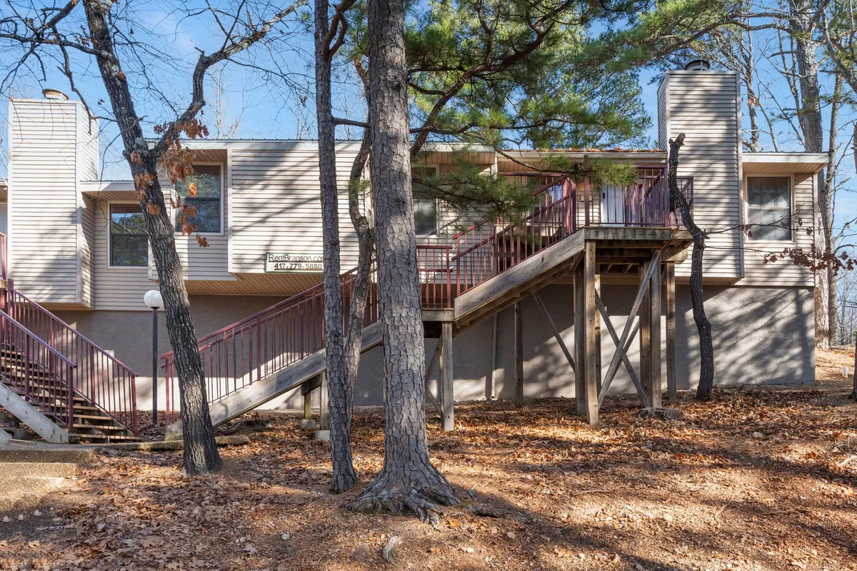This exterior image captures a wooden staircase leading up to the condo building, surrounded by mature trees that create a peaceful, secluded atmosphere. The tranquil scene invites thoughts of morning coffee on the porch while immersed in nature.