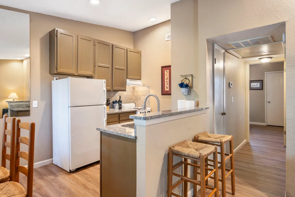 A view of the kitchen counter with stools, a refrigerator, and cabinetry. The setup highlights the modern appliances and spacious counters, making it clear this is a well-equipped, functional kitchen ideal for cooking and entertaining.
