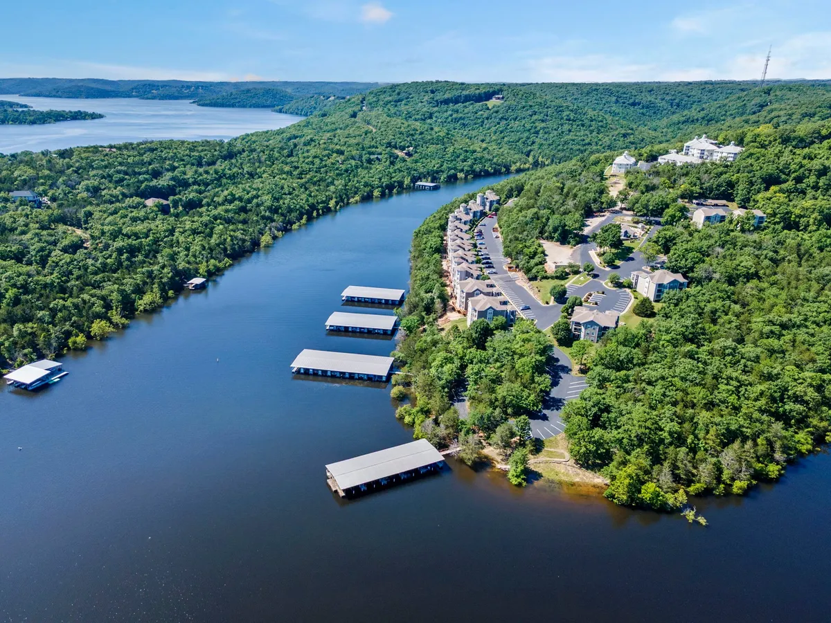 The image captures a peaceful river scene with docks, boats, nearby buildings, and lush greenery. The docks are easily accessible for families looking to swim, fish, or launch boats, and the surrounding nature sets the stage for a variety of aquatic adventures. The calm water and natural backdrop enhance the inviting lakeside atmosphere.