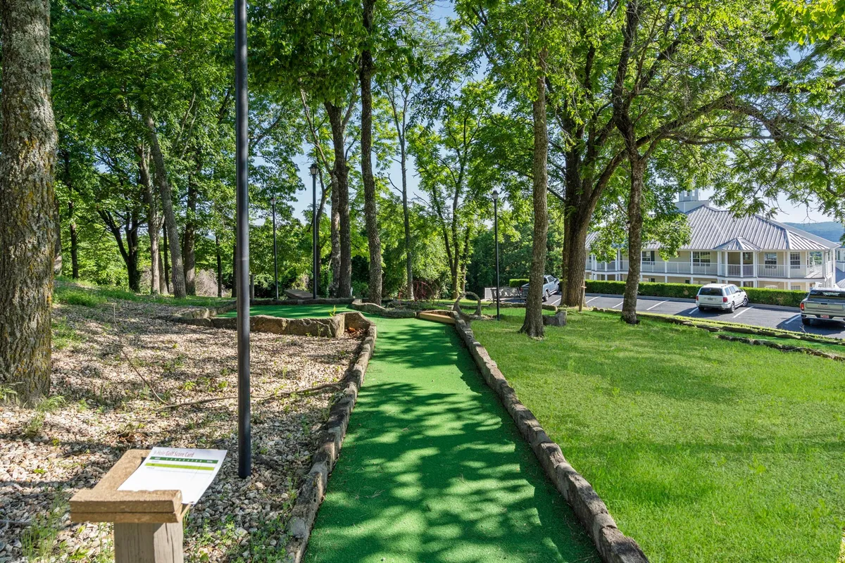 This image spotlights a mini-golf pathway surrounded by lush trees, with clear signage indicating the playful atmosphere. The setting is outdoors, inviting guests into a space designed for family-friendly competitions and casual relaxation.